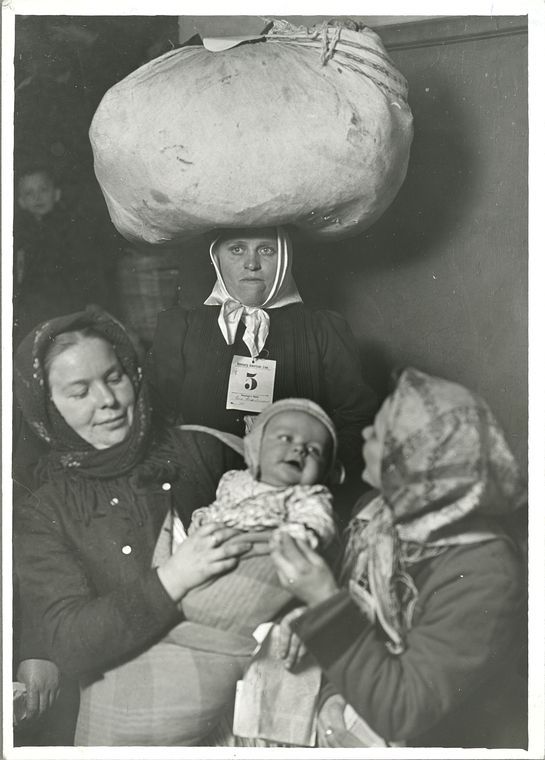 Fotografía de archivo: tres mujeres recién llegadas a Ellis Island, una con un fardo sobre la cabeza y una etiqueta numerada prendida en el pecho, otra sosteniendo a un bebé.