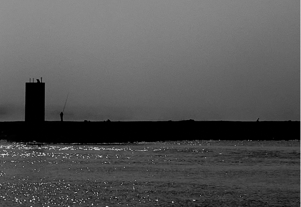«Deriva», imagen liminal: red de pesca, madera astillada y manta térmica dorada en penumbra.