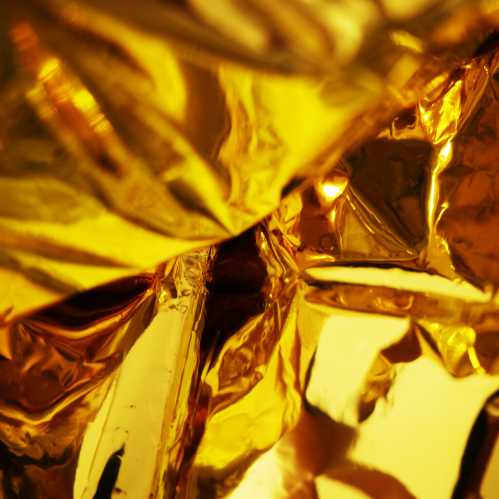 Close-up of a crumpled golden thermal blanket; amber metallized aluminum fills the frame.