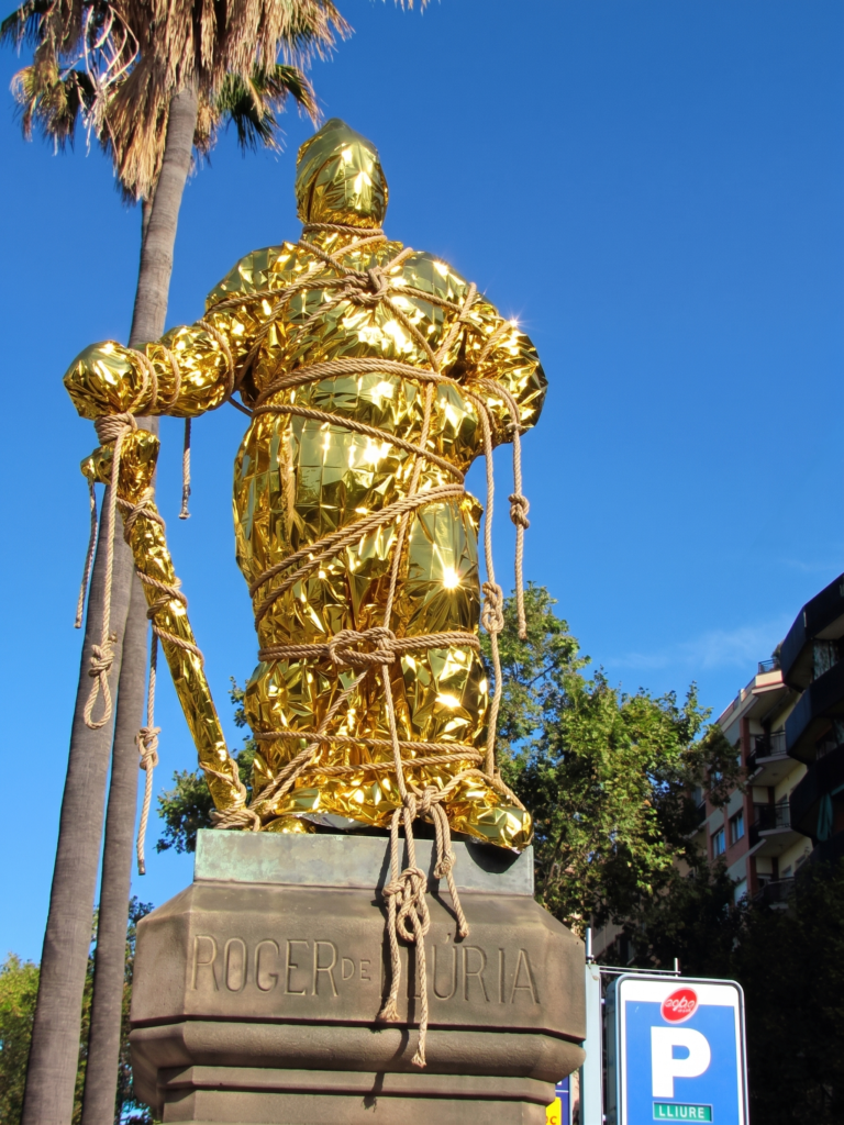 Monument to Admiral Roger de Llúria wrapped in a golden thermal rescue blanket, rope, and sailor's knots.